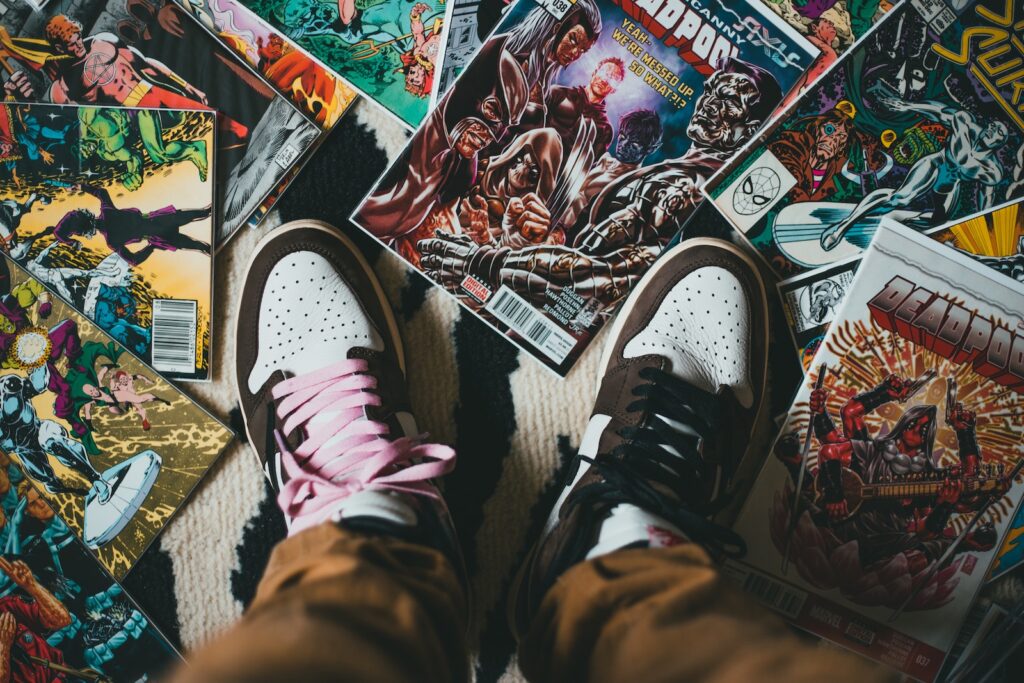 Guardiões da galáxia. From above crop person wearing brown trousers and sneakers standing on pile of collection of comics magazines with colorful illustrations on cover